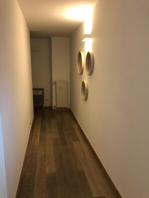 Käytävä, jossa on puulattia, päädyssä ovi ja kolme seinälle kiinnitettyä pyöreää peiliä.
