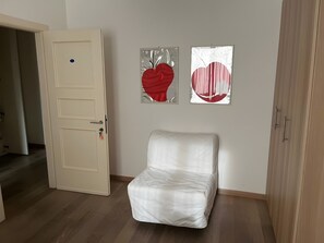 Ein Zimmer mit einem weißen Stuhl, einer Tür und zwei an der Wand befestigten Kunstwerken.