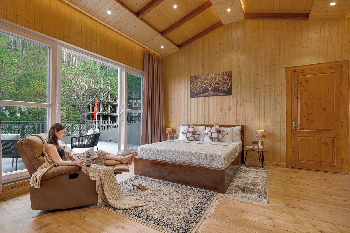 A bedroom with a large window, a bed, a chaise lounge, and a wooden ceiling.