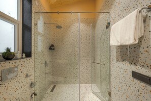 A glass-enclosed shower with a speckled tile wall, a towel hanging on the wall, and a small plant on the windowsill. - ELIVAAS Bask and Blessings 1 Room Suites (Anhech)