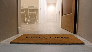 Un couloir avec un paillasson sur lequel est écrit « BIENVENUE », menant à une pièce dotée d’une porte.