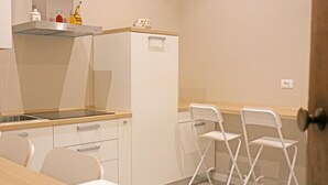 Une petite cuisine équipée d’un évier, d’une cuisinière et d’un réfrigérateur. On y trouve deux chaises blanches et une table.