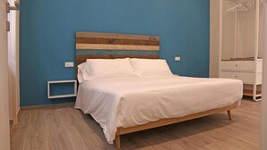 Une chambre à coucher avec une tête de lit en bois, un couvre-lit blanc, une table de chevet blanche et une armoire blanche.