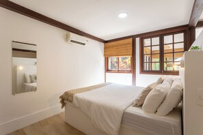 A bedroom with a bed, a window with blinds, a wall-mounted air conditioner, and a mirror. - On the edge of the lagoon-Gigóia Island: tranquility & nature next to the subway (Rio de Janeiro)