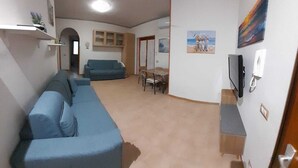 Olohuoneessa on sohva, televisio, kattotuuletin ja seinällä taulu.