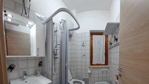 Pieni kylpyhuone, jossa on suihku, kaksi wc:tä, pesuallas ja peili.