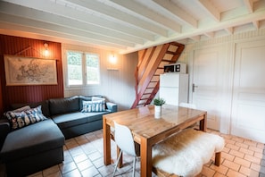 Un salon chaleureux avec un canapé, une table à manger en bois, un banc, un escalier et une porte blanche.