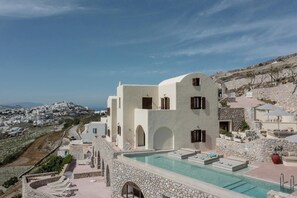 Un bâtiment blanc doté d’une piscine, de murs en pierre et offrant une vue sur une ville située sur une colline.