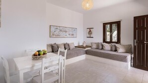 Une pièce avec une table blanche, deux canapés gris, une chaise blanche, un luminaire suspendu et une fenêtre donnant sur un paysage.
