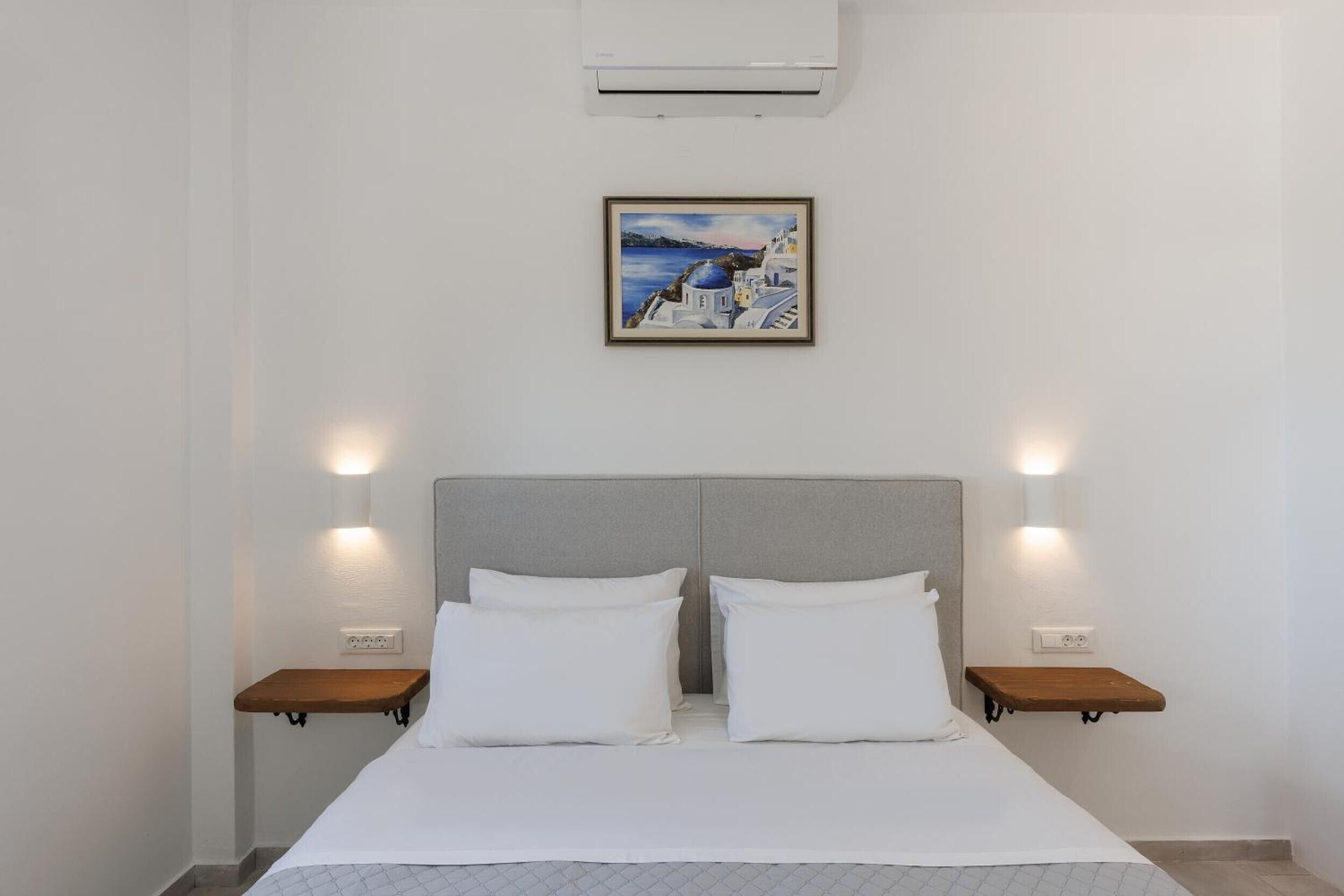 A hotel room with a bed, two bedside tables, a headboard, an air conditioner, and a framed picture on the wall.