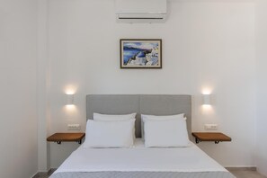 Une chambre d’hôtel avec un lit, deux tables de chevet, une tête de lit, un climatiseur et un tableau encadré au mur.