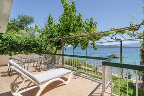 A balcony with a lounge chair, a table, and chairs, overlooking a body of water and mountains. - Secret Beach B Apartment with Sea View, Wi-Fi, and Air Conditioning (Nikiana)
