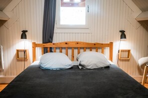 En säng med en sänggavel i trä, två sänglampor och ett fönster med gardiner.