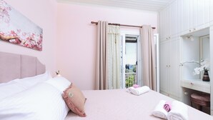 Une chambre à coucher avec un lit, une table de chevet, un miroir et une fenêtre avec des rideaux.