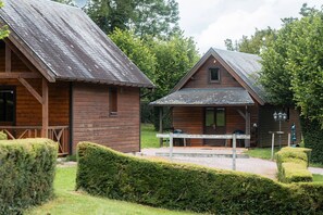 Dos cabañas de madera con techos a dos aguas, un banco y una mesa en primer plano.