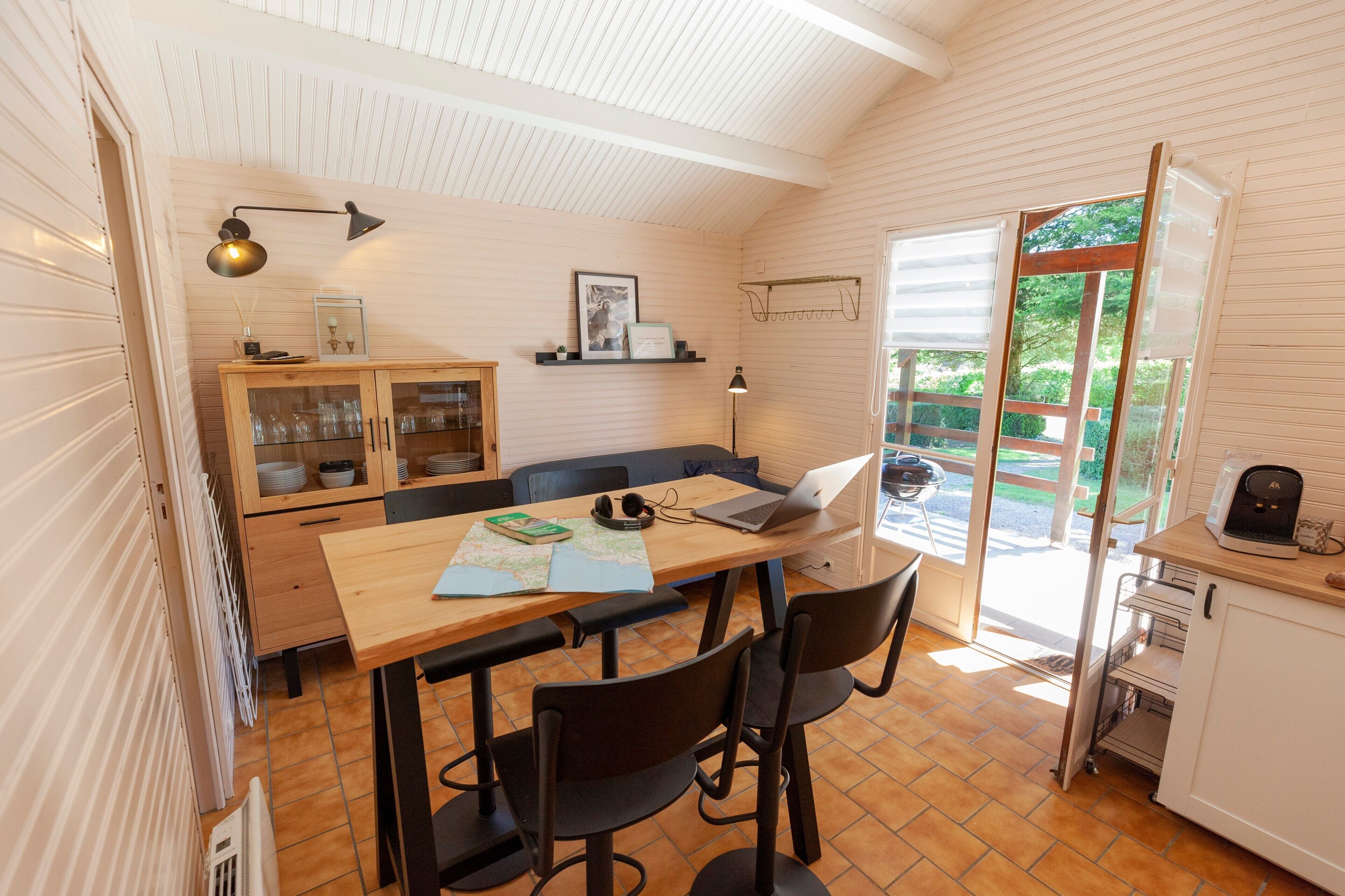 A compact kitchen with a wooden table, chairs, a laptop, and a coffee machine.