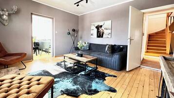 Ein modernes Wohnzimmer mit einer Couch, einem Couchtisch, einem Ledersessel, einem Kuhfellteppich und einem aufgehängten Hirschkopf.