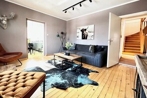 A modern living room with a sofa, a coffee table, a leather armchair, a cowhide rug, and a mounted deer head. - 4 Season Lodge by Belle-Stay for 8 people with a stunning view (Zell am See)
