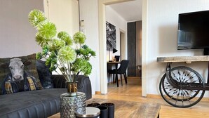 Un soggiorno moderno con un divano, un tavolino da caffè con oggetti decorativi, una televisione e una ruota di bicicletta appesa al muro.