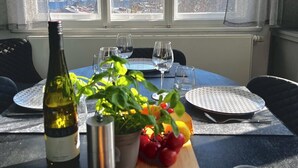 Tavola imbandita per due, con bottiglia di vino, una pianta, frutta e un cesto di pane.