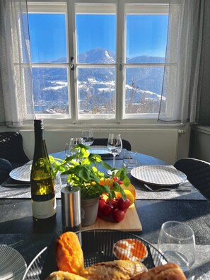 Ein Tisch für zwei, gedeckt mit einer Weinflasche, einer Pflanze, Obst und einem Brotkorb.