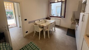 Een kleine, schone kamer met een eettafel, stoelen, een raam met uitzicht en een koelkast.