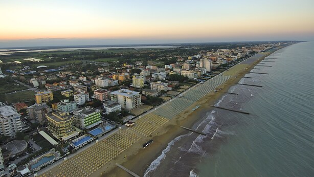 Luchtbeeld van een kustplaats met een lang strand, gebouwen en een heldere lucht.