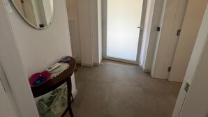 Een gang met een deur aan het einde, een spiegel aan de muur en een klein tafeltje met een bord en een tas.