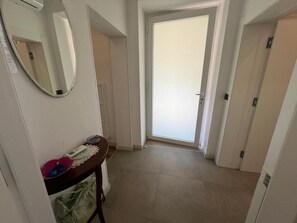 Ein Flur mit einer Tür am Ende, einem Spiegel an der Wand und einem kleinen Tisch mit Teller und Tasche.