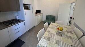 Een compacte keuken met een fornuis, magnetron en een eettafel met een schaal fruit.