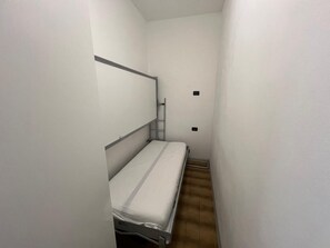 Ein schmaler Raum mit einem Einzelbett, einer steilen Treppe und einem kleinen Regal.