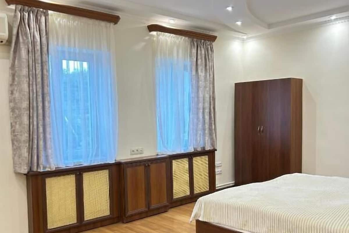 Un dormitorio con suelo de madera, una cama con colcha a rayas, un armario y una ventana con cortinas.