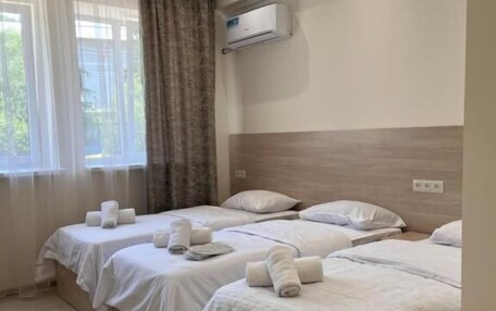 A hotel room with three beds, a window with curtains, an air conditioning unit, and a tiled floor.