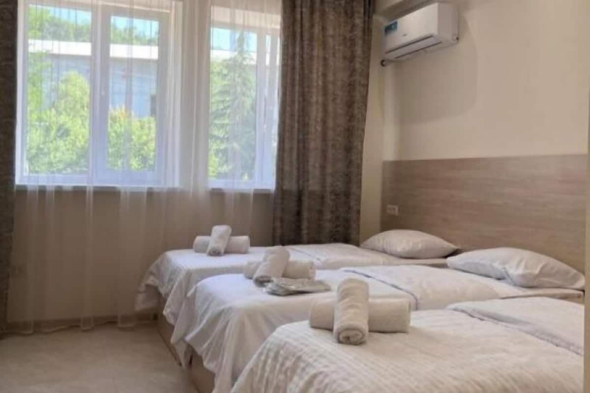 Habitación de hotel con dos camas, una ventana con cortinas, un equipo de aire acondicionado y vistas a zonas verdes.