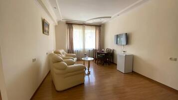 Una sala de estar con un sofá, una mesa de comedor, un televisor y un refrigerador.