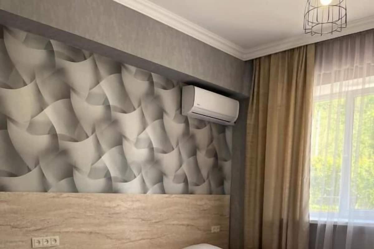 Una habitación de hotel con tres camas, un cabecero moderno y un amplio ventanal con cortinas.