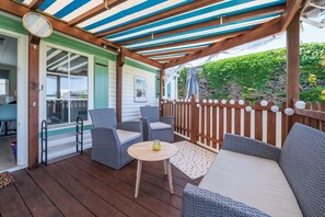 Eine überdachte Terrasse mit Korbmöbeln, einem kleinen Tisch und einer Uhr.