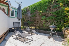 Un patio con dos sillones de descanso, una parrilla y una pared cubierta de vegetación.