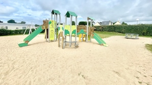 Ein Spielplatz mit Rutsche, Klettergerüsten und einer Schaukel auf sandigem Untergrund.
