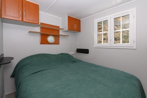 Een slaapkamer met een bed, houten kasten, een raam en een wandplank.
