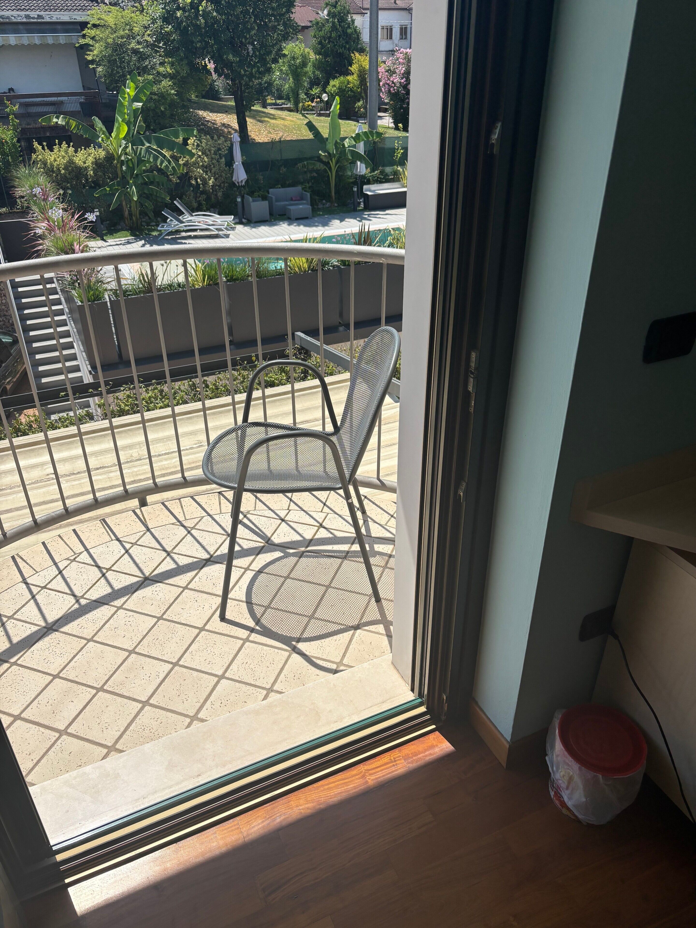 Un balcone con una sedia, un tavolino e vista su una zona residenziale.