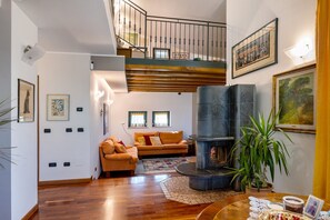 A spacious living area with a fireplace, a sofa set, a staircase, and artwork on the walls. - Homestay 'La Casa Di Gio – Double Room and 2 Singles' – Shared Pool, Wi-Fi & Air Conditioning (Zevio)