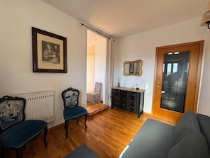 A living room with a sofa, chairs, a wooden cabinet, a framed picture, and a door.