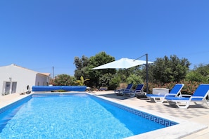 Ein Swimmingpool mit blauen Fliesen, umgeben von Liegestühlen und einem Sonnenschirm.
