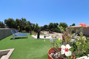 A rooftop garden with artificial grass, two blue lounge chairs, a potted plant with white flowers, and a clear blue sky. - Casa Susanne Country House with Private Pool, Wi-Fi, and Air Conditioning (Tunes)