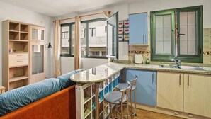 A compact kitchen with a bar counter, stools, a wooden cabinet, and a window with curtains.