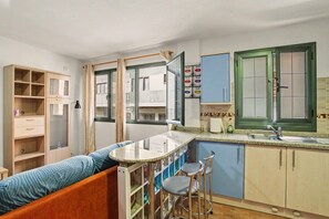A compact kitchen with a bar counter, stools, a wooden cabinet, and a window with curtains.