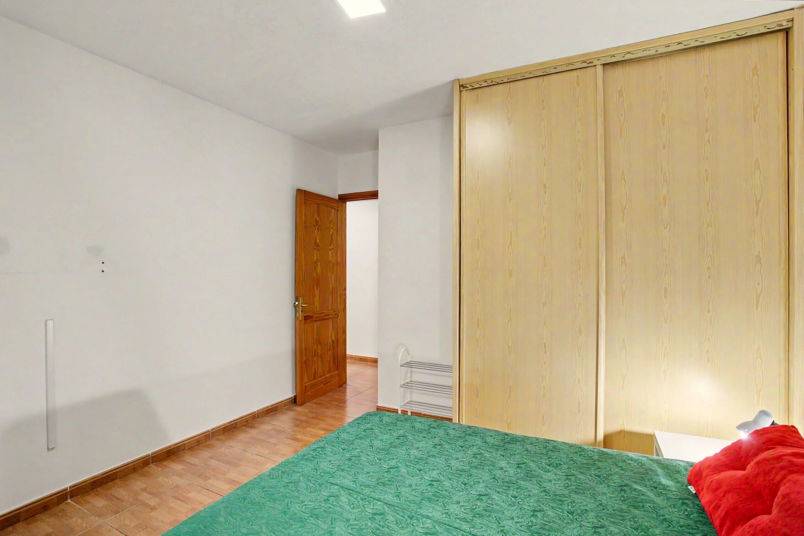 Un dormitorio con cama, armario, puerta y radiador.