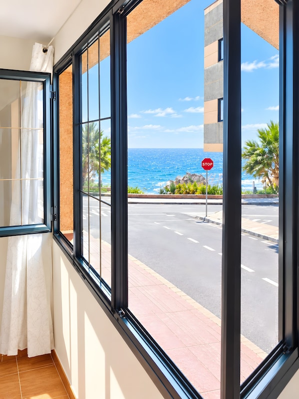 A room with a large window overlooking a street with a stop sign, palm trees, and a view of the ocean.