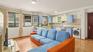 A living room with a sofa, a washing machine, and a kitchen area.